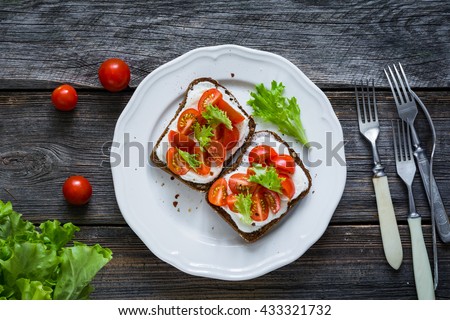 Toast sandwiches with fresh cheese, tomatoes and green salad on a plate. Rustic wooden backdrop, table top view food