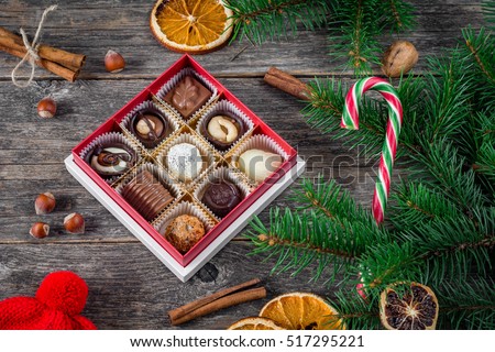 Christmas gifts, Christmas decoration: box of chocolate sweets, candy cane, spices, nuts and dried orange rings on wooden background. Still life of Christmas holidays
