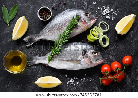 Fresh uncooked dorado or sea bream fish with lemon slices, spices, herbs and vegetables. Mediterranean cuisine. Top view