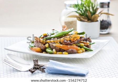Stir-fried mixed vegetables with pork in square dish on white mat background.