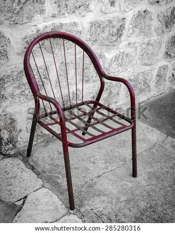 Old red metal chair beside stone wall, Montenegro