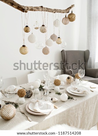 Festive living room decorated for Christmas and New Year with stylish table set for four person and vintage Christmas decoration hanging above it.