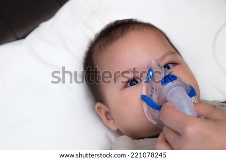 5 months old baby with respiratory disease, inhaling medication through spacer while laying in hospital bed