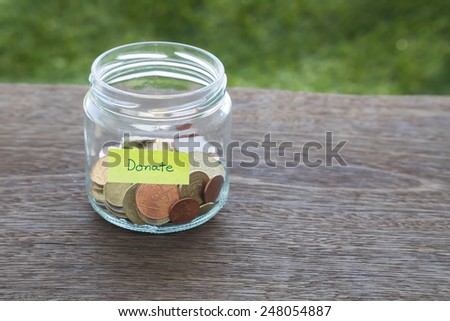 World coins in money glass jar with DONATE word label place on natural wood table, blank space for text