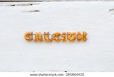 The upper-case letters word CALCIUM. Alphabet cookie crackers putting on rough texture of white wood background.