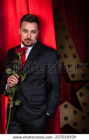 a young and handsome man in a business suit with a red background and with a rose in hand