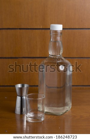 Small glass of Vodka on a wooden table with a bottle and measuring cup