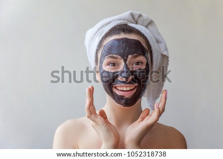 Beauty portrait of a smiling brunette woman in a towel on the head applying black nourishing mask on face on white background isolated. Skincare cleansing spa relax cosmetics concept