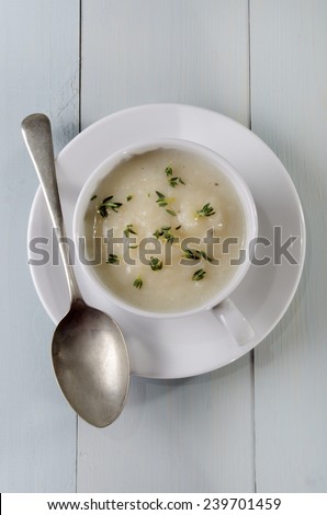 home made creamy cauliflower soup in a cup with thyme on wood