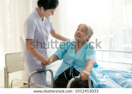 Asian young nurse supporting elderly patient disabled woman in using walker in hospital. Elderly patient care concept.