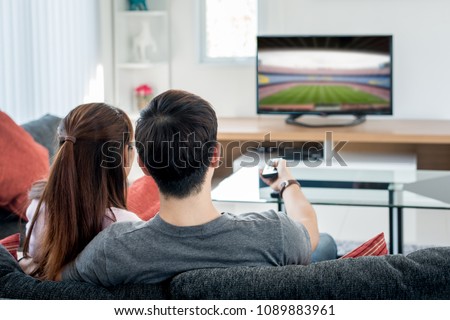 Rear view of Asian couple watching football at television in living room. Football festival concept.