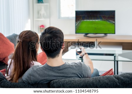 Rear view of Asian couple watching football at television in living room. Football concept.