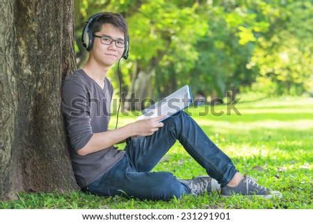 Young student in park listening to music on headphones