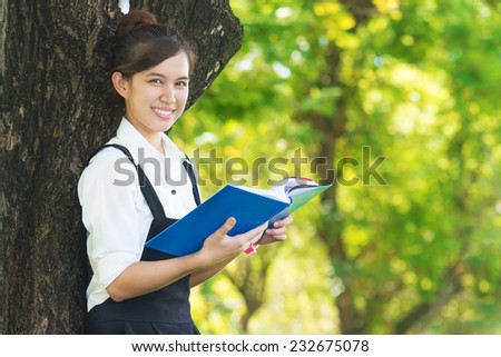 Student reading book in park, standing under a tree. Relaxing outdoors reading.
