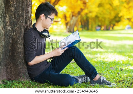 Man reading book in park, sitting under a tree. Relaxing outdoors reading.