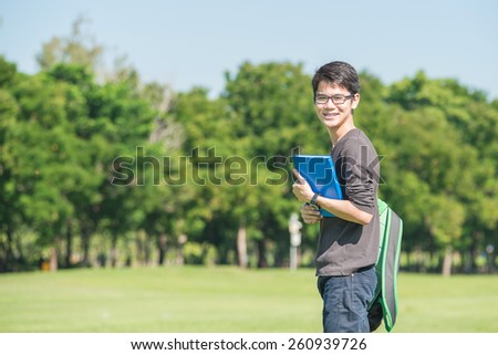 Asian student holding books and smiling while standing in park at college