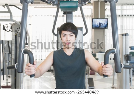 Asian man having fitness training in gym to build up muscle on a weight machine