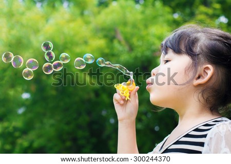 Asian little girl blowing soap bubbles in green park