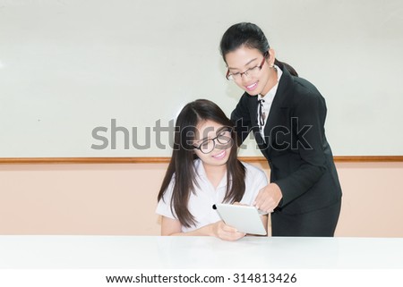 Asian teacher assisting student using digital tablet at desk in classroom