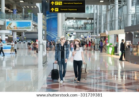 Asian couple tourist with wheel luggage at the international airport.
