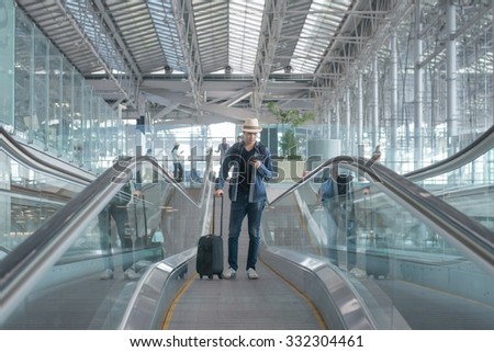 Young Asian man with luggage down the escalator in airport.