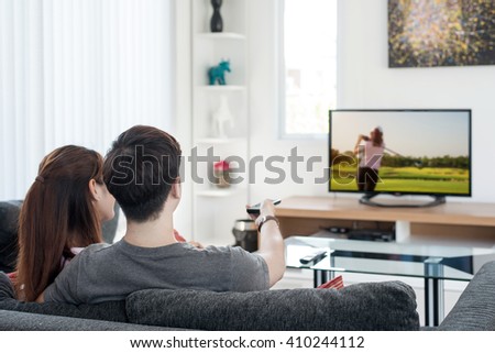 Sport, Golf, People concept - Young Asian couple watching golf sport on tv at home. Asian couple looking enjoy golf sport game.