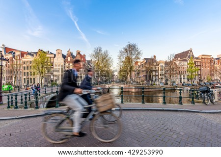 People bicycling through city streets on a beautiful summer day in Amsterdam, Netherlands.