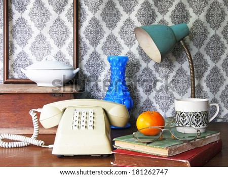 still life with Push Button Telephone,orange,vase,lamp,old book,glasses and tea cup on wooden table.