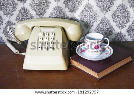 still life with old book,tea cup and Push Button Telephone on wooden table.