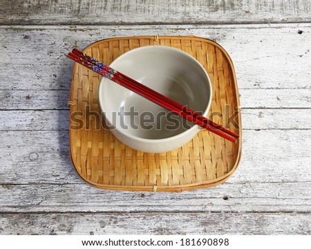 ceramic bowl and chopsticks in bamboo tray on wooden table.