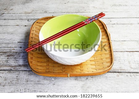 ceramic bowl and chopsticks in bamboo tray on wooden table.