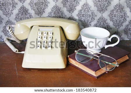 still life with old book,Push Button Telephone,glasses and tea cop on wooden table.