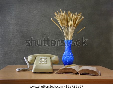 still life with Push Button Telephone,vase of flowering grass and old book on wooden table.