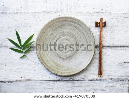 ceramic dish (plate) and chopsticks on white wooden table.Flat lay