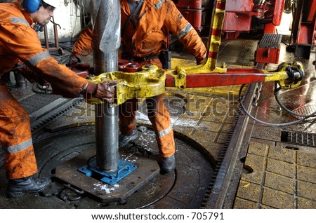 Two roughnecks breaking a connection with help from tongs. Offshore oil rig.