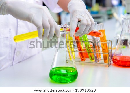 Scientist pour test tube in erlenmeyer flask Scientist pour test tube in erlenmeyer flask