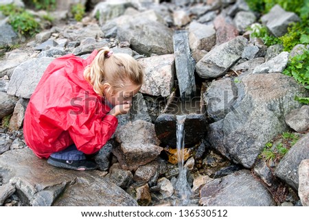 Thirsty girl drinking water from mountain stream