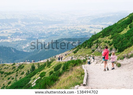 Woman and girl on mountain trail. Landscape with trail on  mountain range and town in valley