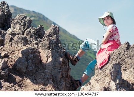 Woman sitting on mountain summit. Slope and blue sky in background