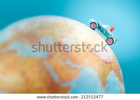 Toy car on the globe on plain blue background. Space for text