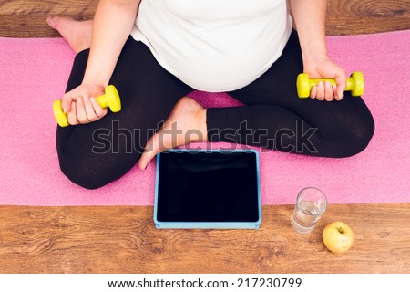 Active pregnant woman with dumbbells exercising with video course