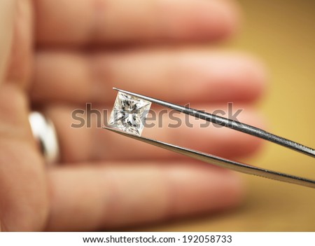 Princess cut diamond in hand held within diamond tweezers