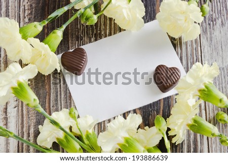 white carnations, chocolates and white sheet of paper. love message