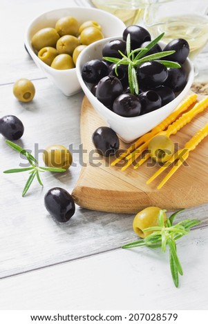 olives in bowls, rosemary and olive oil on a cutting board on the table.selective focus. health and diet