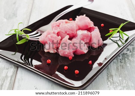 pieces of raw meat and fresh rosemary on a black plate.health and diet food