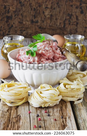 minced meat in a bowl and the ingredients for making pasta dishes on the old wooden table. european cuisine