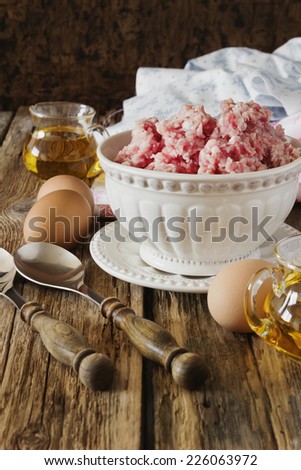 minced meat in a bowl and different ingredients on an old wooden table.meat dishes