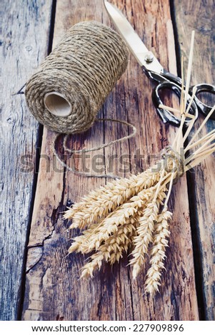 bunch of wheat ears, old scissors and a skein of linen thread on an old wooden table. stories of rural life