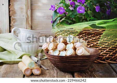 wafer rolls with cream, basket with flowers and coffee cups. sweet breakfast