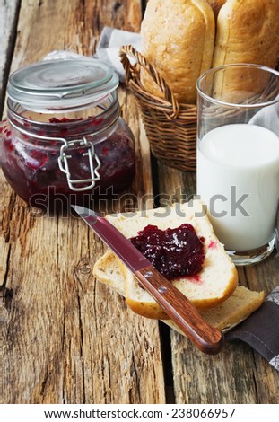 bun with seasoning in a basket, a glass of fresh milk and cherry jam on old wooden table. simple rustic food.